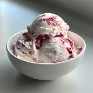 Two scoops of creamy cottage cheese ice cream with a berry swirl in a white bowl.