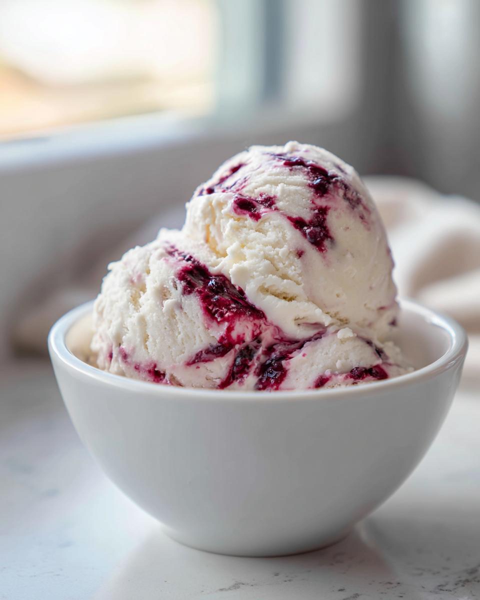 A white bowl filled with creamy cottage cheese ice cream, swirled with a vibrant berry sauce.