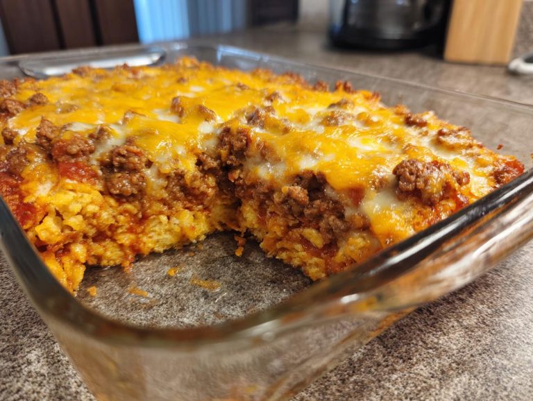 Close-up of a cheesy Dorito Casserole in a glass baking dish, showing layers of chips, meat, and melted cheese.