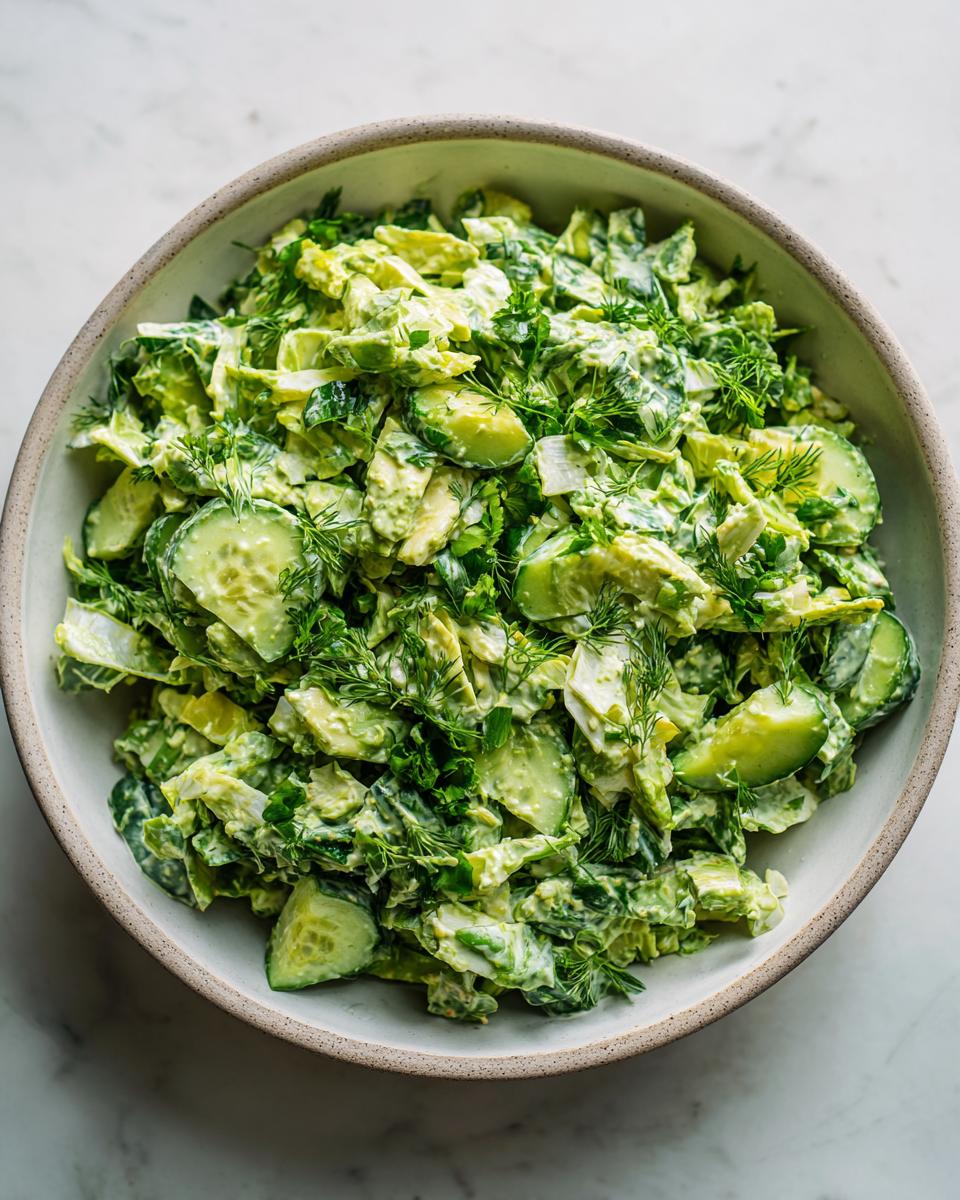 Overhead shot of a bowl filled with vibrant Green Goddess salad, featuring fresh greens, cucumber, and herbs.