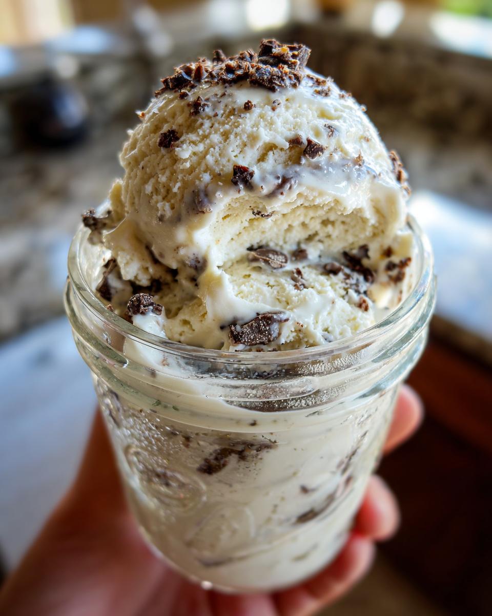Close-up of creamy mason jar ice cream with chocolate chunks, held in a hand.