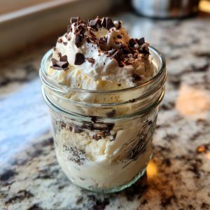 A mason jar filled with creamy vanilla mason jar ice cream and topped with whipped cream and chocolate chunks.