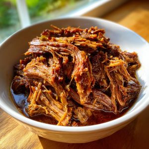 Close-up of shredded Mississippi pot roast in a white bowl, glistening with savory juices.