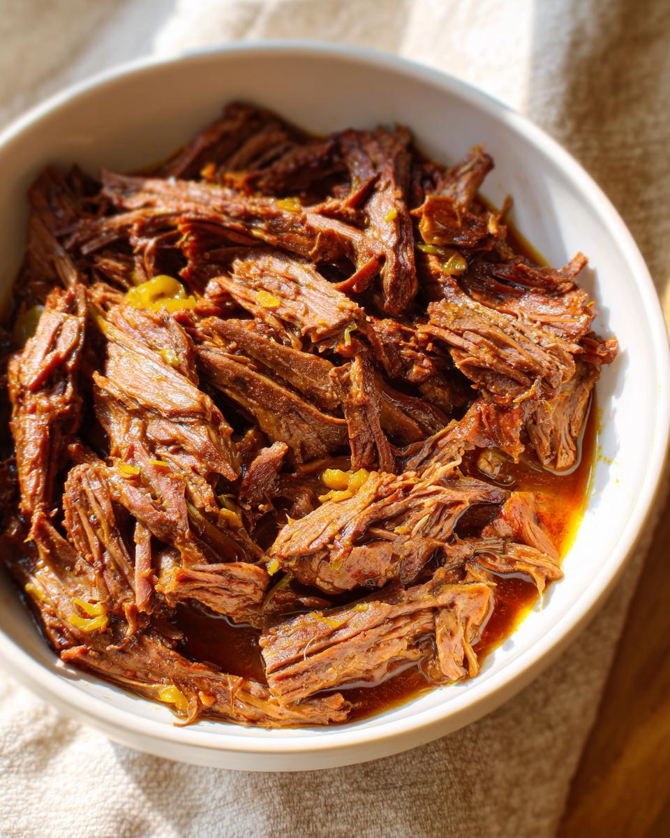 A close-up of shredded Mississippi pot roast in a white bowl, glistening with savory juices.