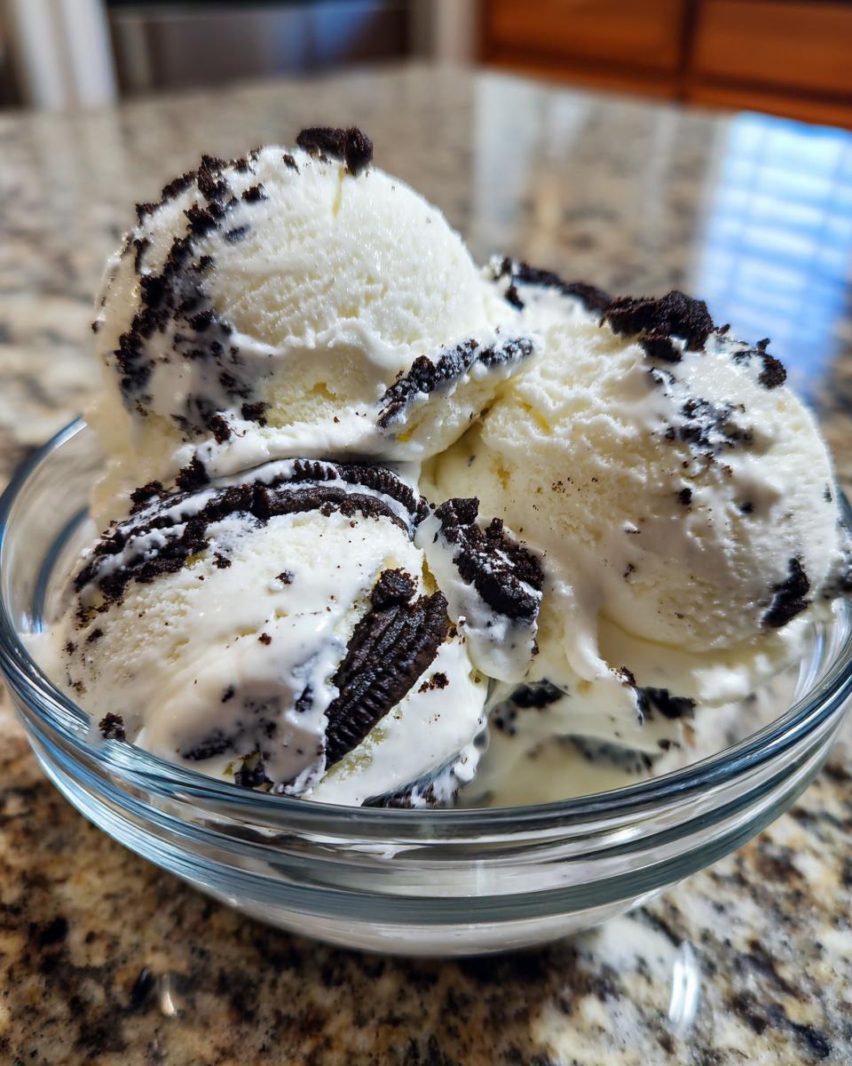 A glass bowl filled with scoops of no churn Oreo ice cream, topped with crushed Oreo cookies.
