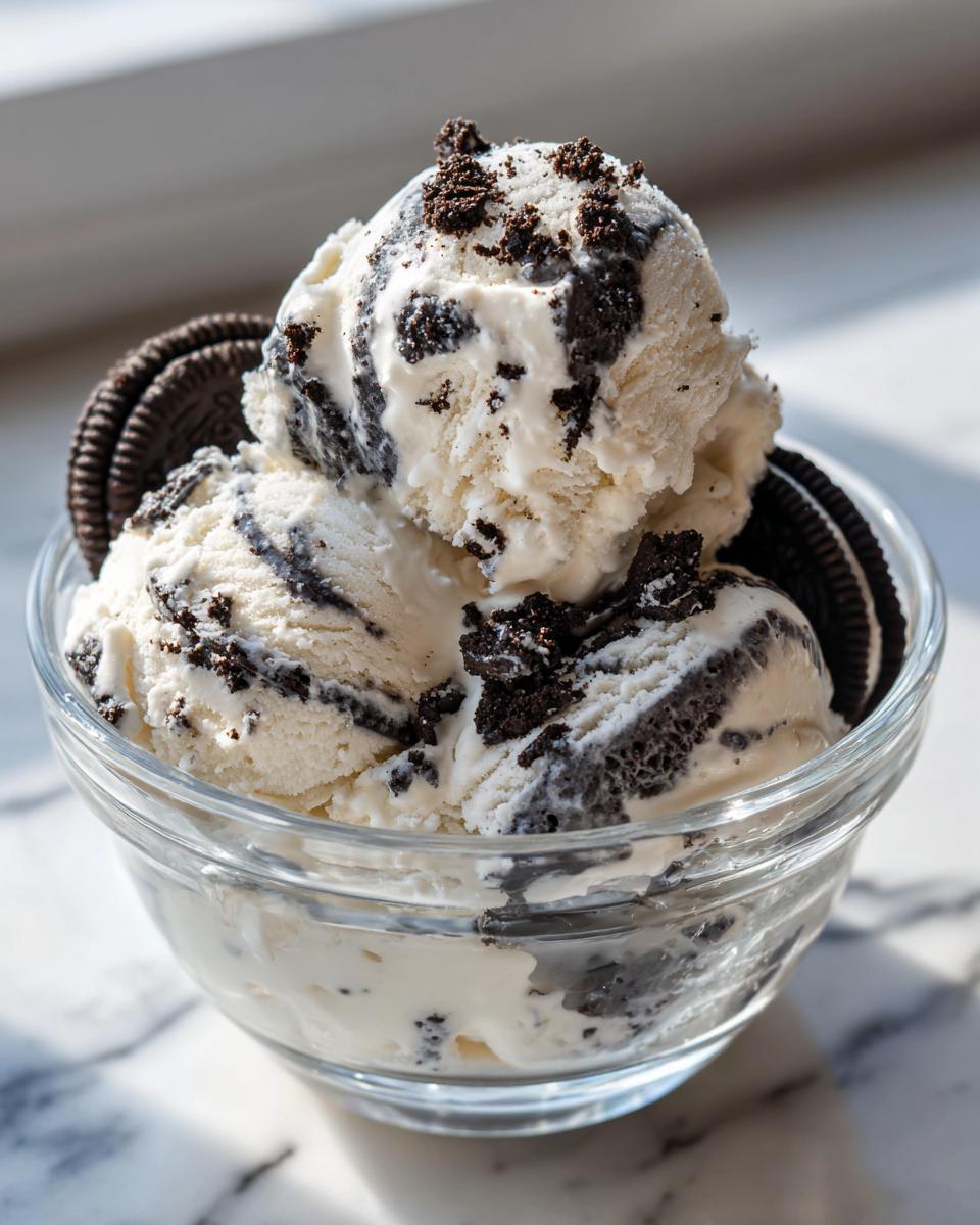 A glass bowl filled with scoops of no churn Oreo ice cream, topped with crushed Oreos and whole cookies.