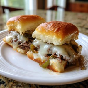 Two Philly Cheesesteak Sliders on a white plate, featuring beef, cheese, and peppers.