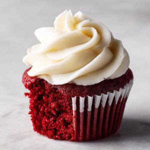 A close-up of a bakery-perfect red velvet cupcake with a bite taken out, showcasing the rich red cake and creamy white frosting.