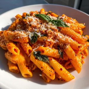 Close-up of creamy spicy vodka pasta with penne, basil, parmesan, and red pepper flakes.