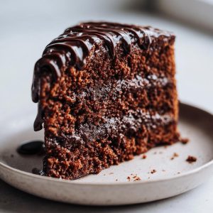 A decadent slice of Vegan Chocolate Cake with rich chocolate ganache dripping down the sides.