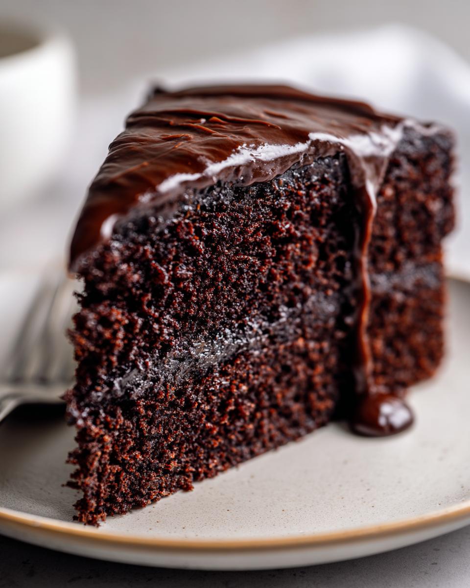 A slice of rich Vegan Chocolate Cake with chocolate ganache dripping down the side.
