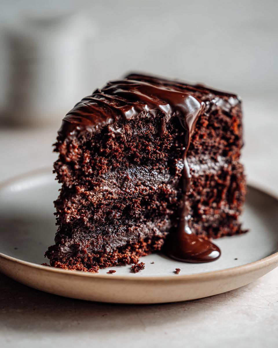 A decadent slice of Vegan Chocolate Cake topped with rich chocolate ganache, served on a plate.