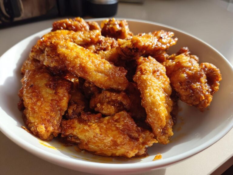 A white bowl filled with golden-brown, crispy air fryer chicken wings coated in a glossy sauce.