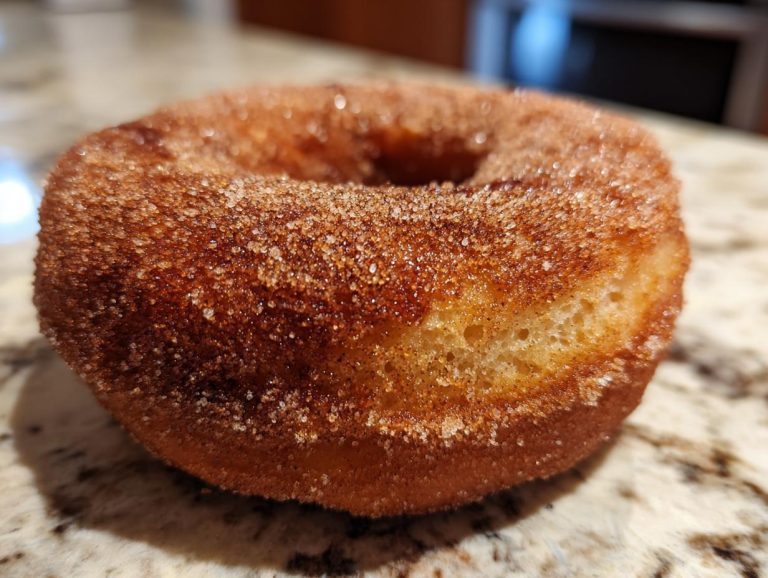 Close-up of a golden-brown baked apple cider donut coated in cinnamon sugar.