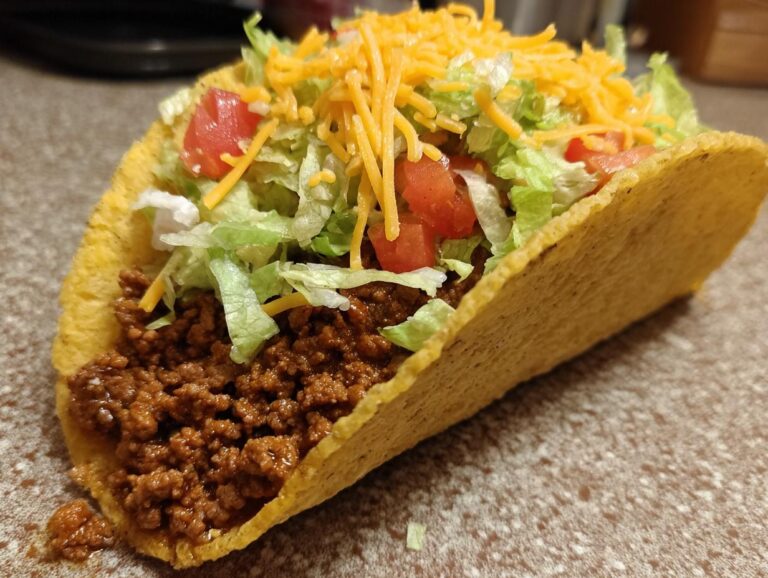 A close-up of a delicious beef taco filled with seasoned ground beef, shredded lettuce, diced tomatoes, and shredded cheese.