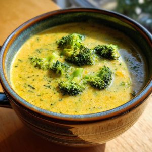 A close-up of a steaming bowl of creamy broccoli cheddar soup topped with fresh broccoli florets.