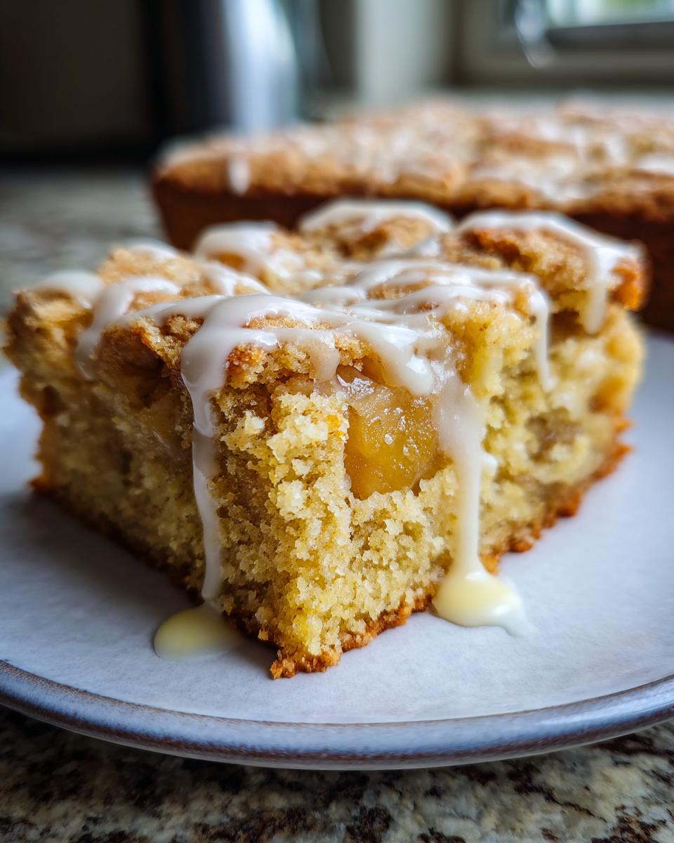 A close-up of a slice of chewy brown butter apple blondies, drizzled with white icing.