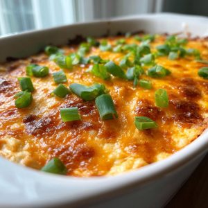A close-up of bubbly, cheesy buffalo chicken dip topped with fresh green onions in a white baking dish.