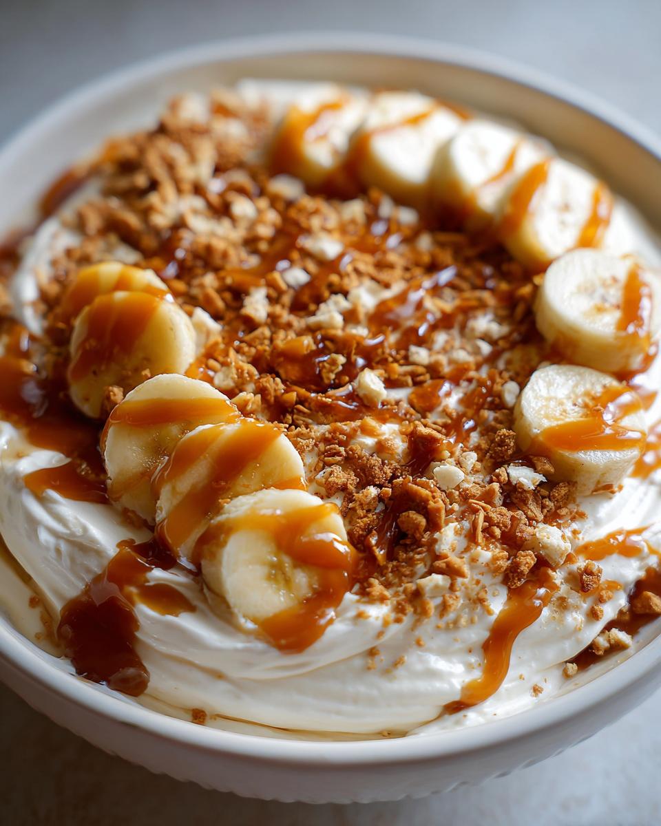 Close-up of a creamy caramel apple dip topped with sliced bananas, cookie crumble, and caramel drizzle.