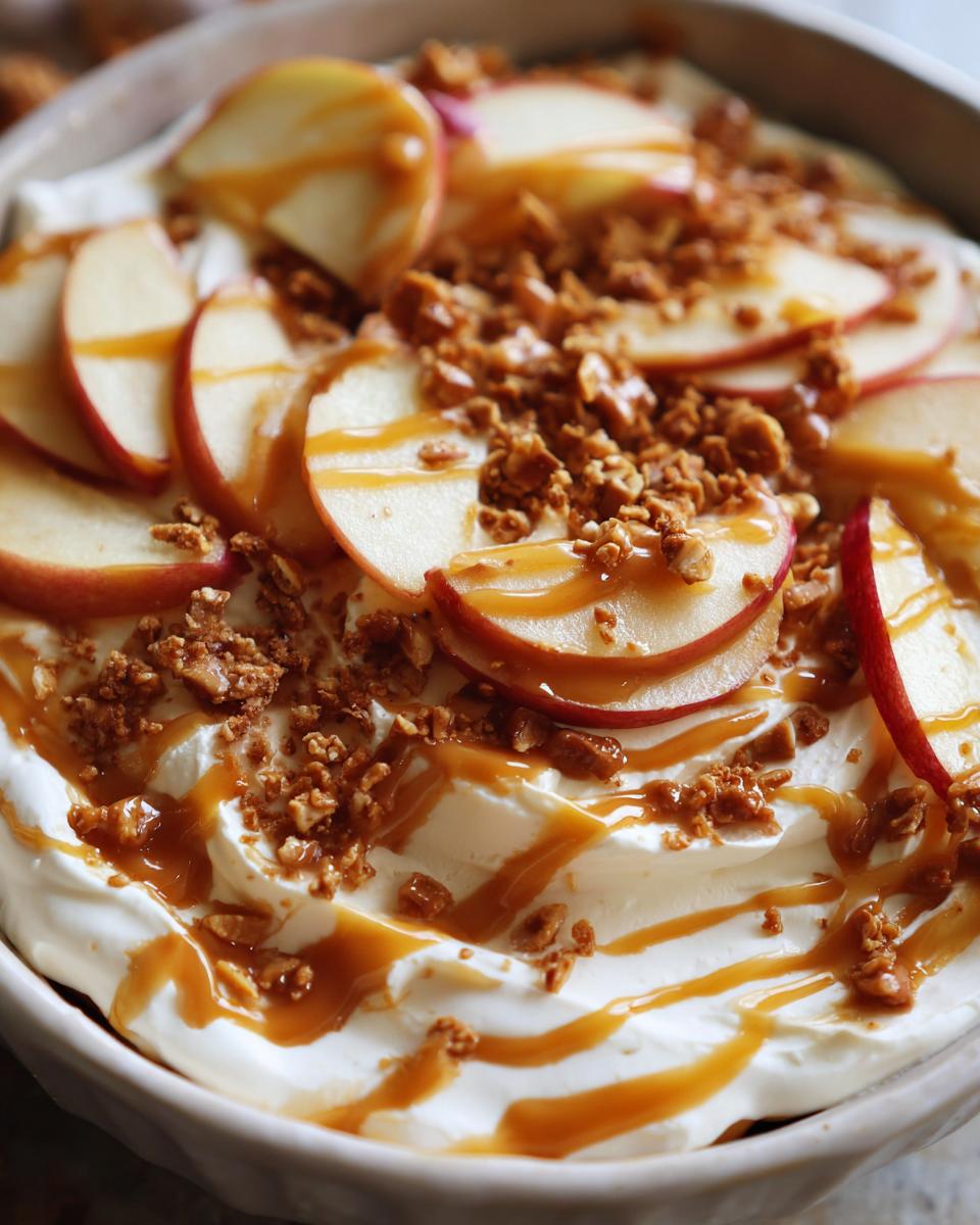 Close-up of a creamy caramel apple dip topped with fresh apple slices, caramel drizzle, and crunchy crumble.