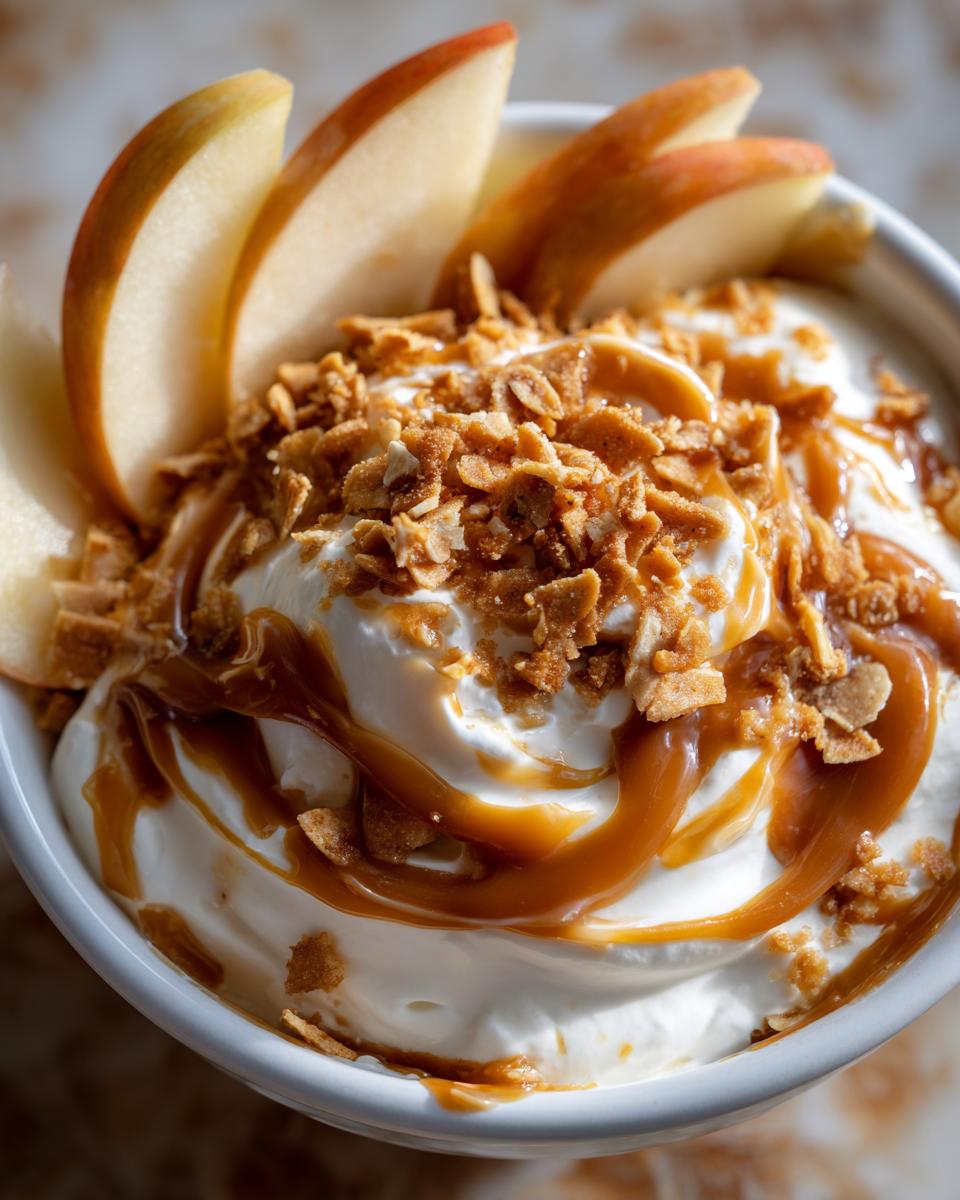 Close-up of creamy caramel apple dip topped with crunchy crumble and drizzled with caramel sauce, garnished with apple slices.