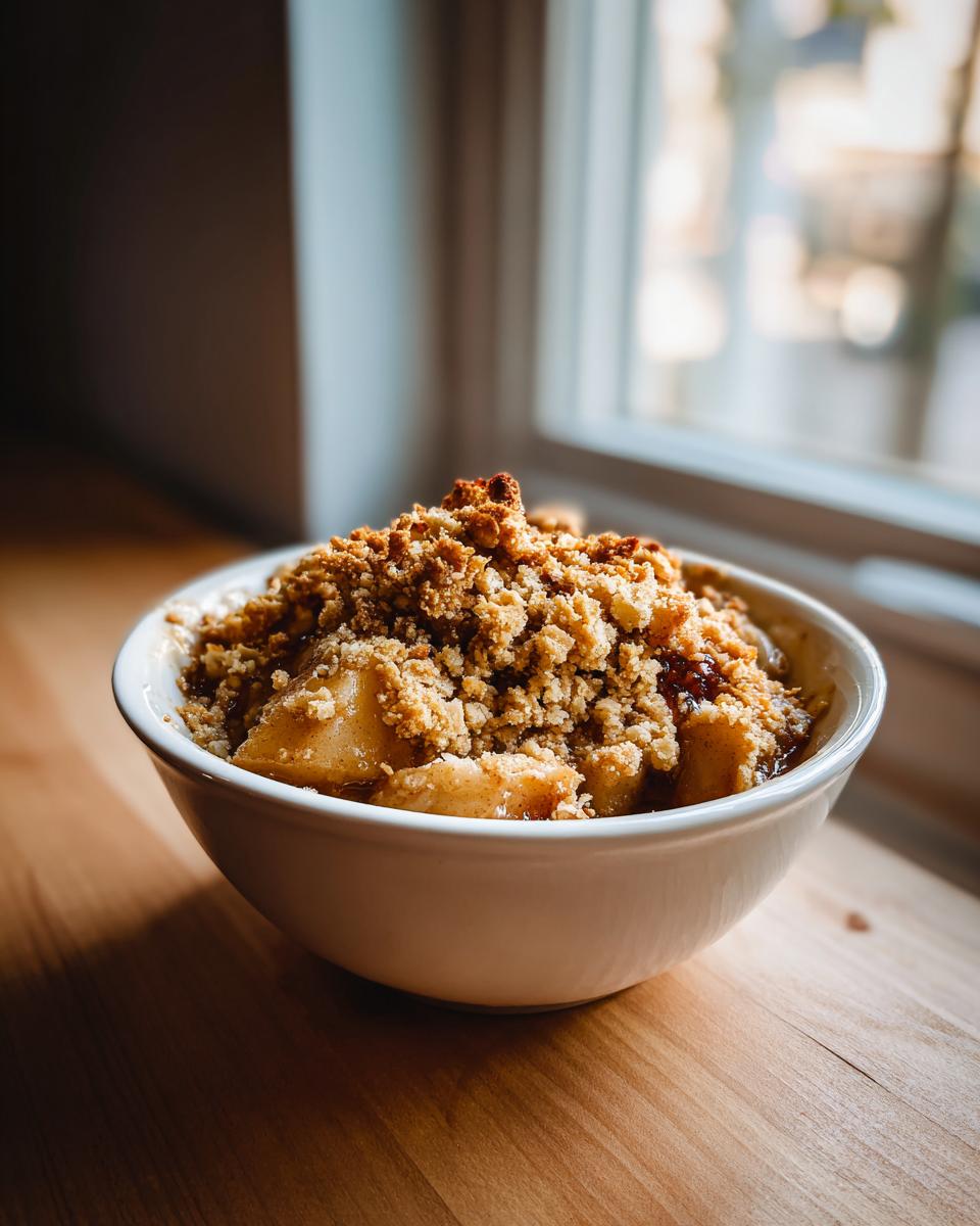 A close-up of a white bowl filled with a serving of easy apple crisp, showing baked apples and a crumbly topping.