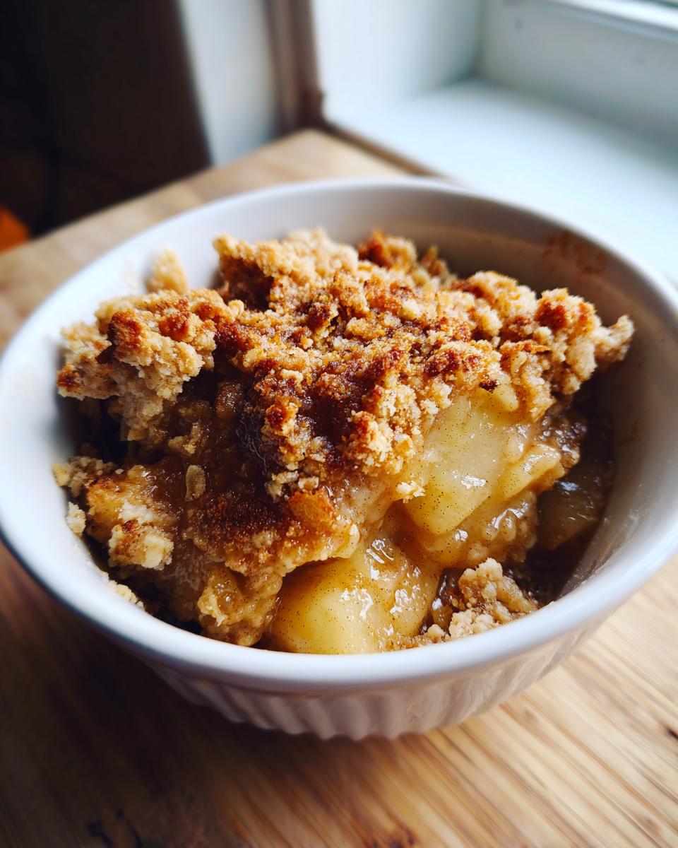 A close-up of a white bowl filled with delicious easy apple crisp, showing tender baked apples and a crunchy crumb topping.