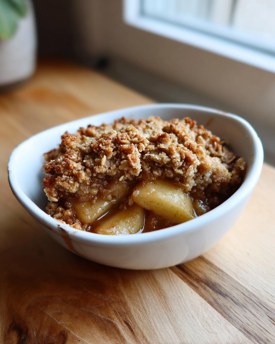 A close-up of a white bowl filled with delicious easy apple crisp, featuring tender baked apples and a golden brown crumble topping.