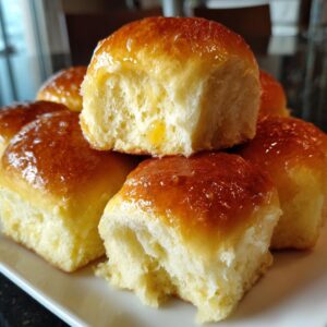 Close-up of a stack of fluffy dinner rolls with a shiny, golden-brown glaze.
