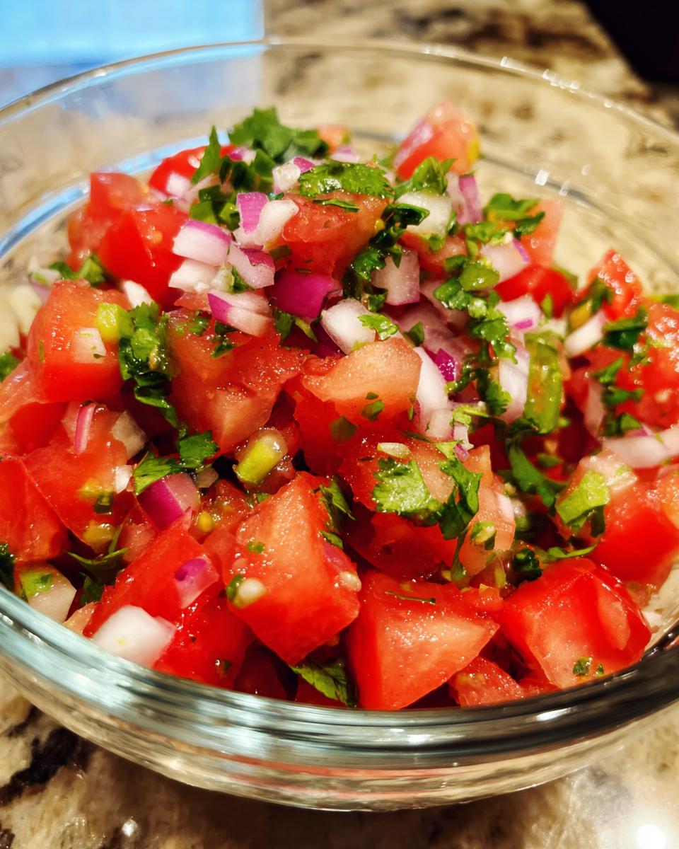 Close-up of a clear glass bowl filled with fresh, vibrant salsa, featuring diced tomatoes, red onion, cilantro, and jalapeño.