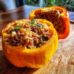 Two halves of a bright orange bell pepper stuffed with a savory mixture of ground beef and rice, garnished with fresh herbs.