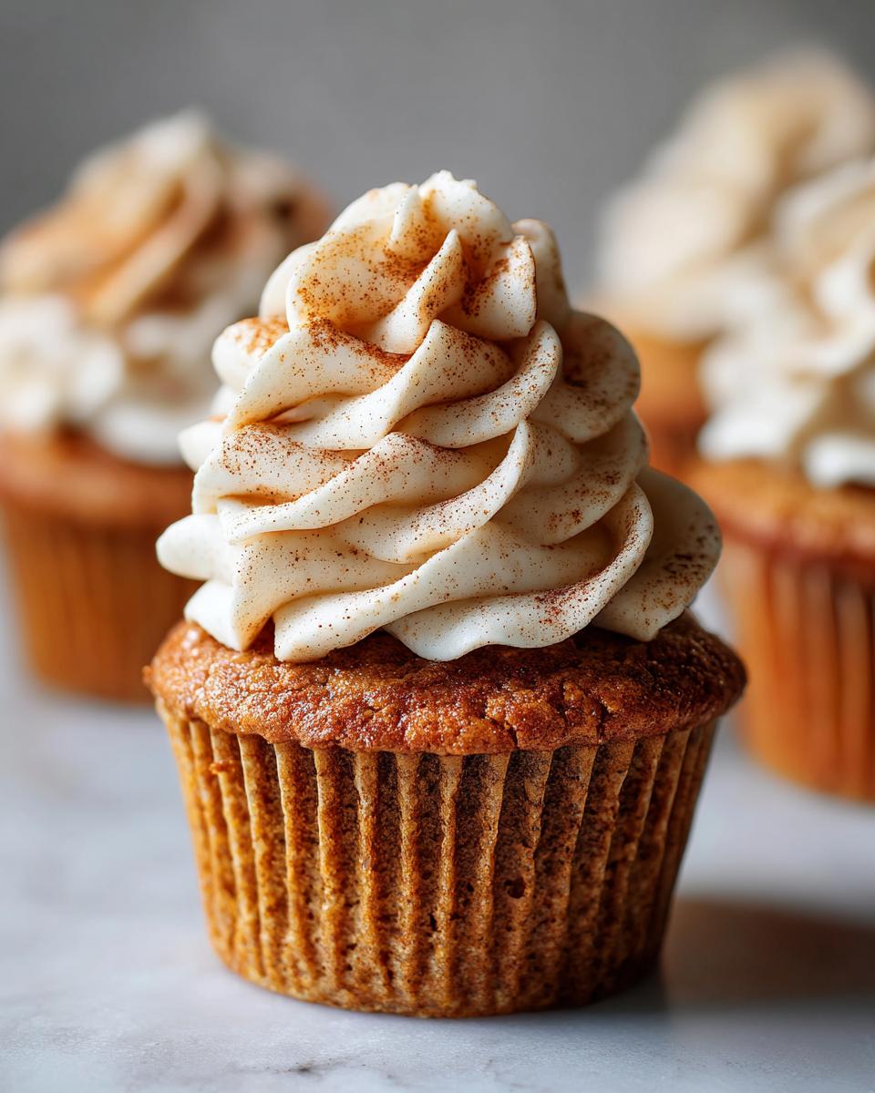 Close-up of a delicious pumpkin spice latte cupcake topped with creamy frosting and a sprinkle of cinnamon.