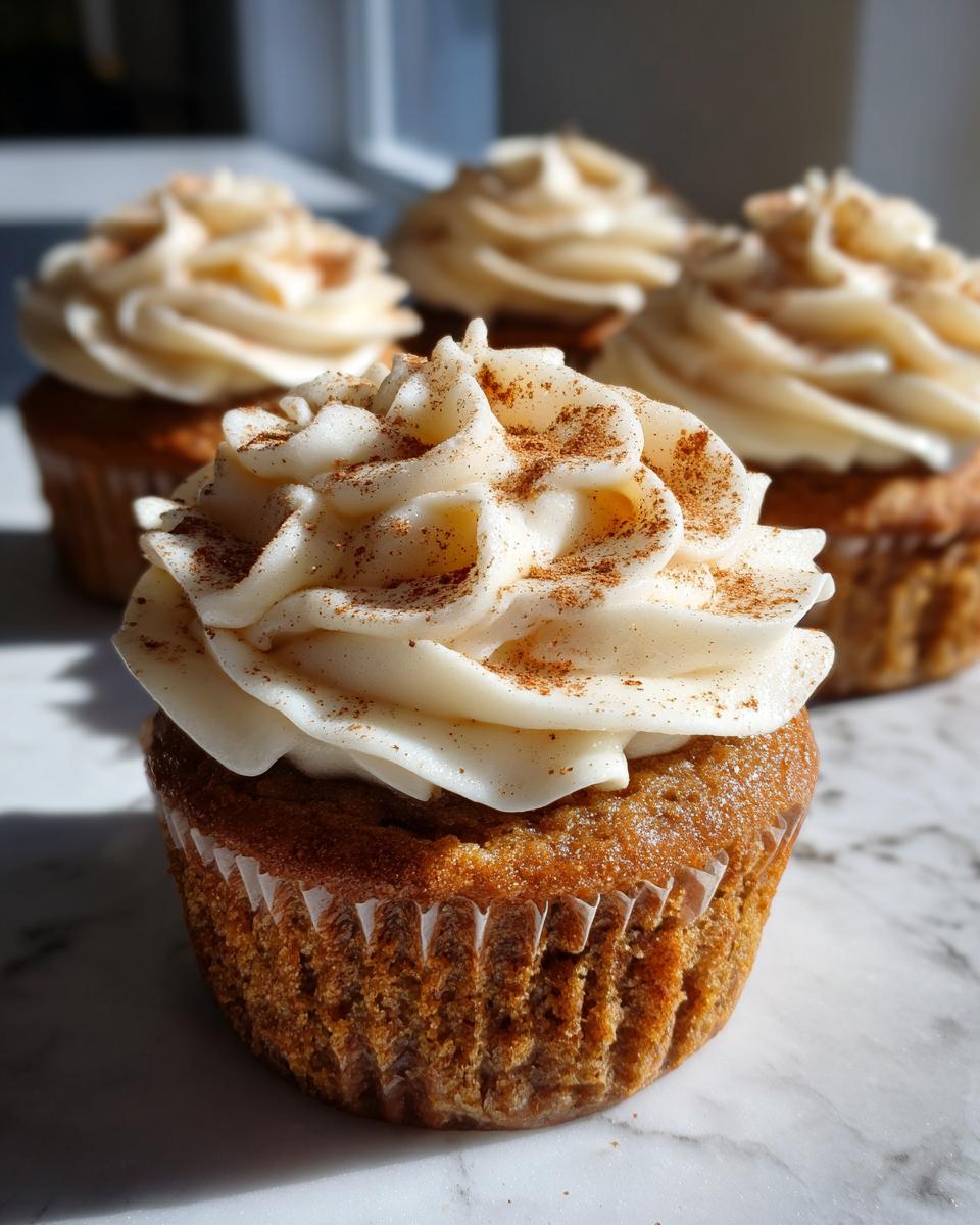 Close-up of a delicious Pumpkin Spice Latte Cupcake topped with creamy frosting and a sprinkle of cinnamon.