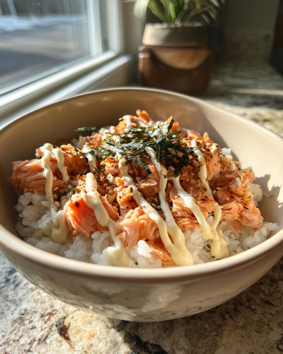 A close-up of a salmon rice bowl topped with shredded salmon, seaweed, sesame seeds, and a drizzle of mayonnaise.