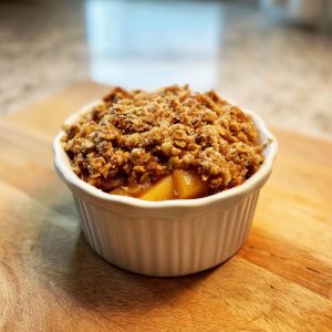 A close-up of a single serving of warm slow cooker apple crisp in a white ramekin, topped with a crunchy oat and nut crumble.