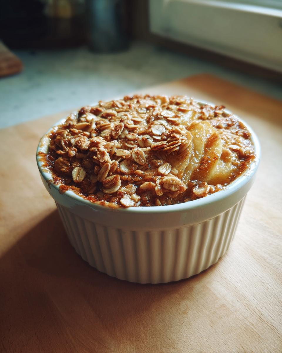A single serving of warm slow cooker apple crisp in a white ramekin, topped with oats and cinnamon.