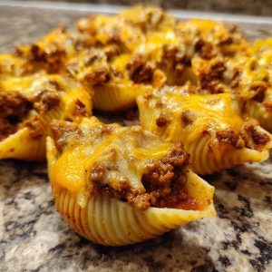 A close-up of several baked taco stuffed shells, generously filled with seasoned ground beef and topped with melted cheddar cheese.