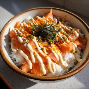 A delicious salmon rice bowl topped with creamy mayonnaise, nori, and green onions.