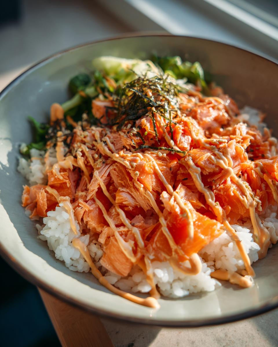 A close-up of a viral salmon rice bowl topped with flaked salmon, creamy sauce, and nori.