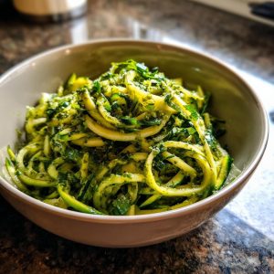 A close-up of a bowl filled with vibrant zucchini noodles tossed in green pesto sauce.