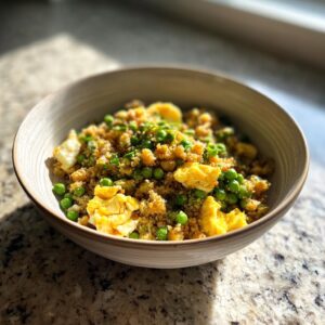 A bowl of delicious Cauliflower Fried Rice with scrambled eggs and green peas, a healthy takeout alternative.