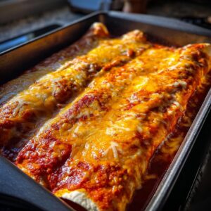 Close-up of cheesy chicken enchiladas baked in a pan with red sauce.