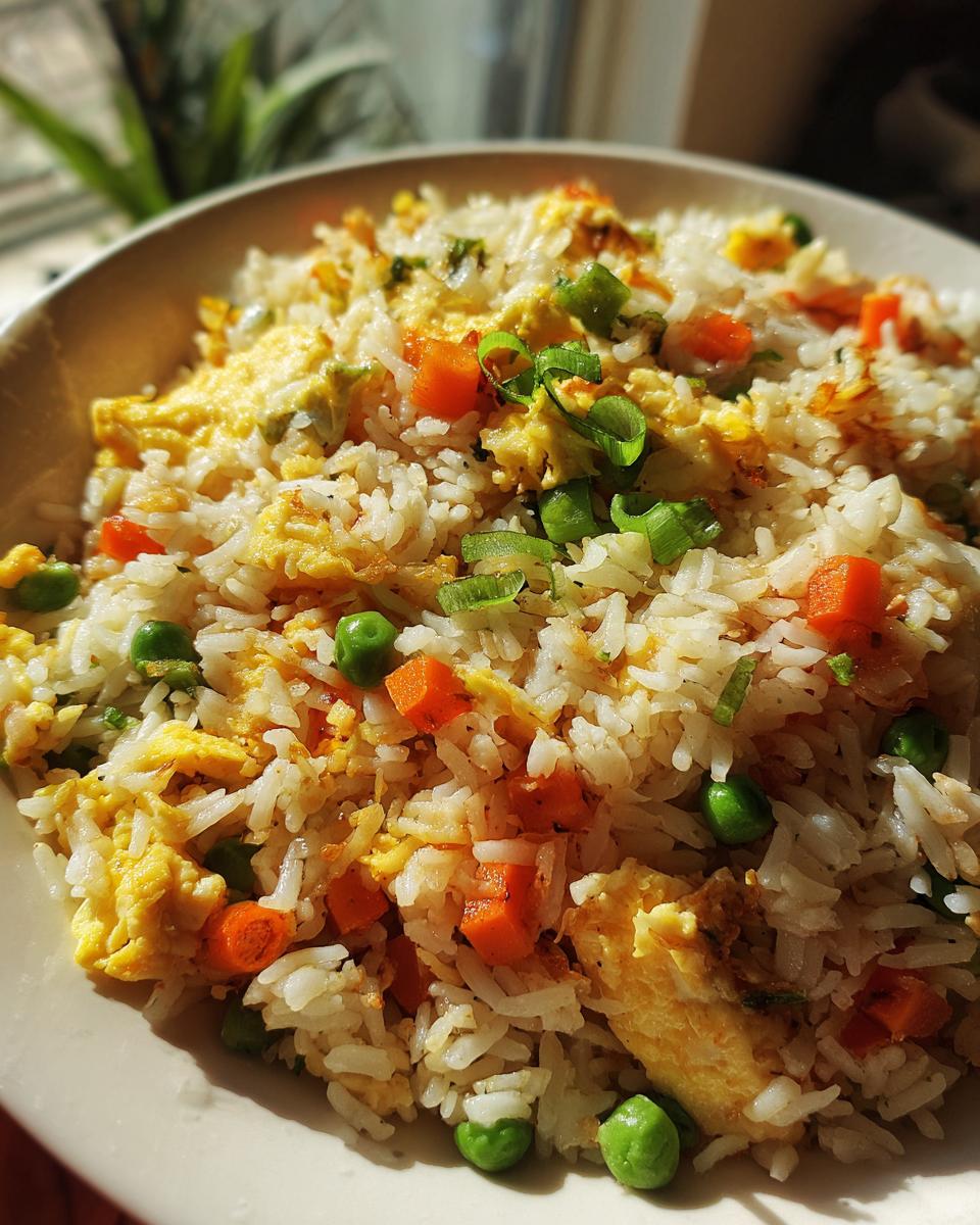 A close-up of a bowl of fluffy fried rice with scrambled eggs, diced carrots, peas, and green onions.