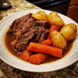 A close-up of a hearty plate of Grandma's amazing pot roast, served with tender potatoes and carrots in rich gravy.