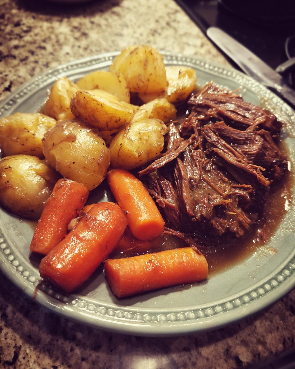 A plate of tender shredded pot roast served with roasted potatoes and carrots.