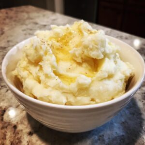 A white bowl filled with fluffy Instant Pot mashed potatoes, topped with melted butter and a sprinkle of seasoning.
