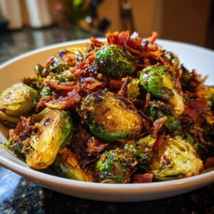 A close-up of roasted Brussels sprouts topped with crispy bacon bits in a white bowl.