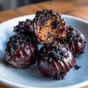 Close-up of fudgy Oreo balls coated in chocolate and crushed Oreos, one is broken open.