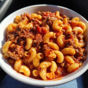 A close-up of a bowl filled with hearty goulash, featuring tender elbow macaroni mixed with seasoned ground beef and a rich tomato sauce.