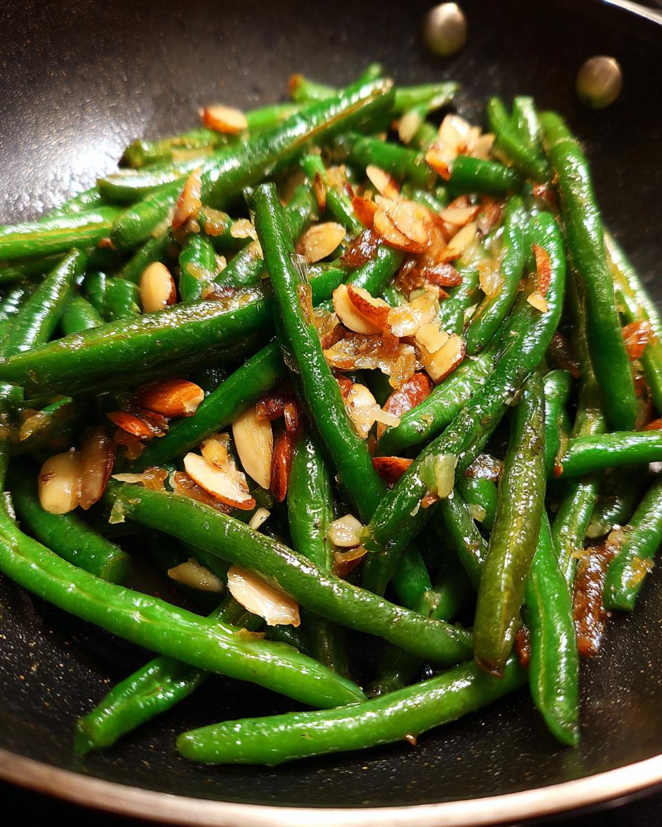 Close-up of vibrant green beans almondine cooked in a pan with toasted slivered almonds.
